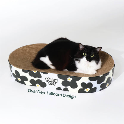 A Tuxedo Cat nesting on top of Oval Den Cat Scratcher Board Bloom Design.