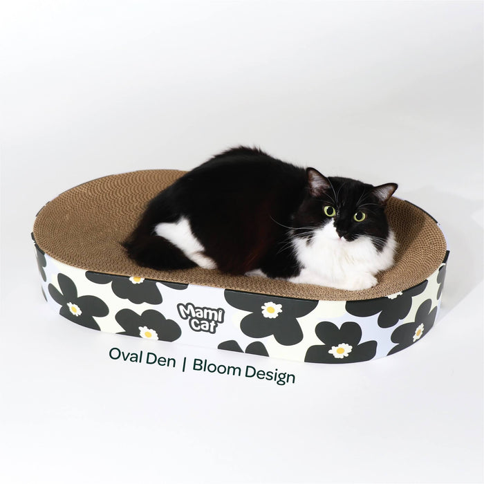 A Tuxedo Cat nesting on top of Oval Den Cat Scratcher Board Bloom Design.
